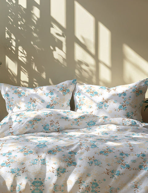 Floral patterned bedding set with light blue flowers on a white background, sunlight casting shadows.