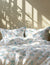 Floral patterned bedding set with light blue flowers on a white background, sunlight casting shadows.