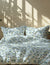 Patterned bedding set with geometric design on a bed in a room with sunlight filtering through a window.