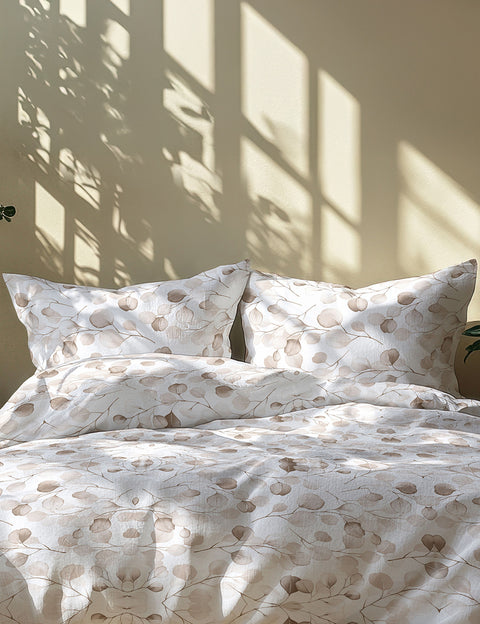 Patterned bedspread with pillows on a bed in a room with sunlight filtering through a window.