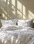 Patterned bedspread with pillows on a bed in a room with sunlight filtering through a window.