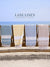 Four towels of various colors hanging on a rack with a scenic ocean view, featuring the 'Lane Linen' brand.