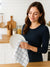 Woman in a kitchen holding a plate and a dishcloth of white color with grey stripe in a kitchen background