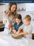 A Woman holding white & grey stripe Kitchen Towel and two children in a kitchen mixing ingredients in a bowl.