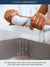 Person holding a white dish cloth with water dripping from it, against a blurred background, the high quality cotton fabric used in the manufacturing of our dish cloths makes them highly absorbent