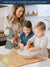 A Woman and two children in a kitchen mixing ingredients in a bowl.