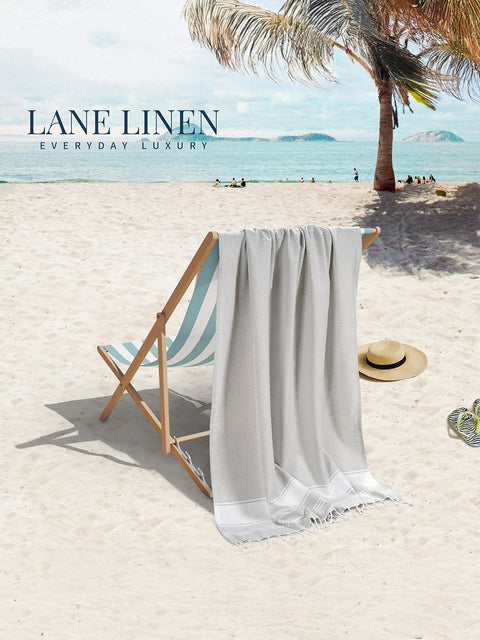 Grey towel hanging over a beach chair on a sandy beach with palm trees and clear blue sky in background