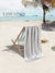 Grey towel hanging over a beach chair on a sandy beach with palm trees and clear blue sky in background