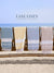 Four towels hanging on a rack with 'Lane Linen' branding against a beach background.
