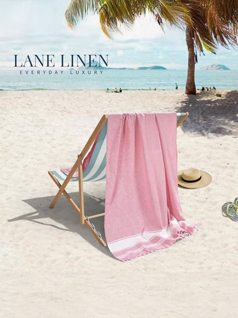 Pink towel draped over a beach chair on a sandy beach with palm trees and clear blue sky in background