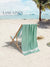 Green towel draped over a beach chair on a sandy beach with palm trees and clear blue sky.