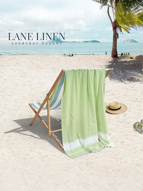 Green towel draped over a beach chair on a sandy beach with palm trees and clear blue sky.