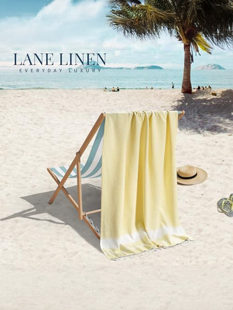 Beach scene with a yellow towel draped over a chair, palm tree, and ocean view with 'Lane Linen' branding.