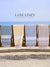 Four towels of different colors hanging on a rack with 'Lane Linen' branding against a beach background.