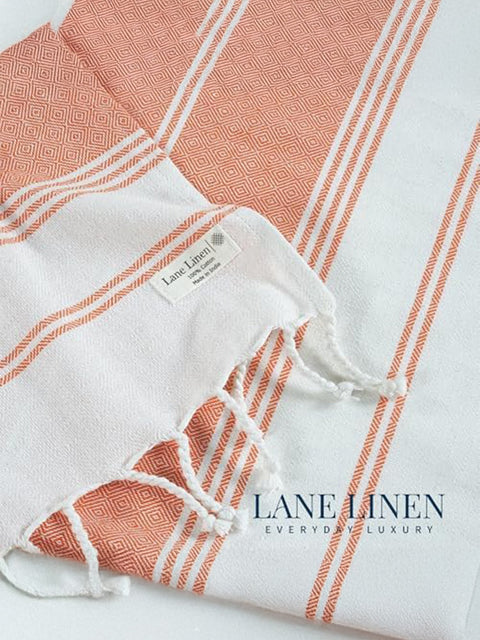Close-up of a white towel with orange stripes and geometric patterns, branded 'Lane Linen'.