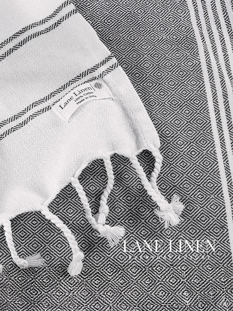 White towel with black stripes and tassels on a geometric patterned background, featuring the brand 'Lane Linen'.
