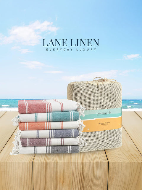 Stack of colorful towels with a woven basket on a wooden surface, against a blue sky background. Brand 'Lane Linen' visible.