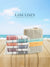 Stack of colorful towels with a woven basket on a wooden surface, against a blue sky background. Brand 'Lane Linen' visible.