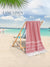 Red Color Beach Towel With White Strips Displayed on A Beach Backgorund hanging on a wooden deck chair
