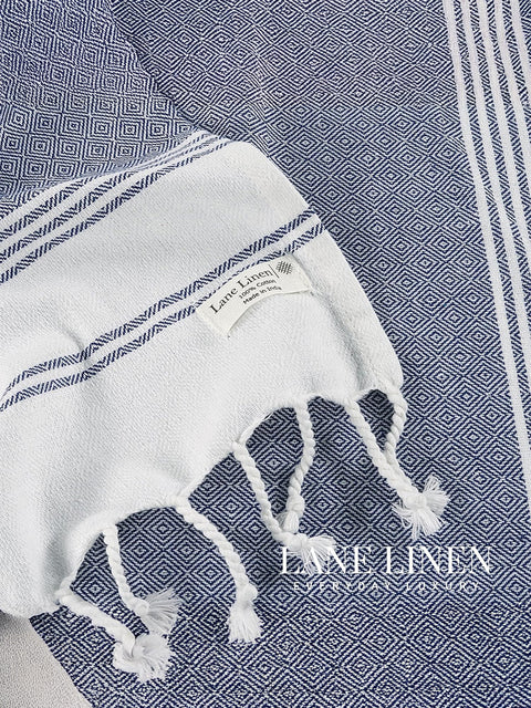 White towel with blue stripes and on a geometric patterned fabric background, featuring the brand 'Lane Linen'.