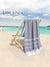 Gray towel with white stripes hanged over a wooden chair on a beach, with 'Lane Linen' branding.