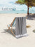 Smoky Black towel draped over a beach chair on a sandy beach with palm trees and ocean in the background, featuring 'Lane Linen' branding.