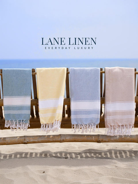 Four towels in blue, beige, and pink hanging on a wooden rack with 'Lane Linen' branding.