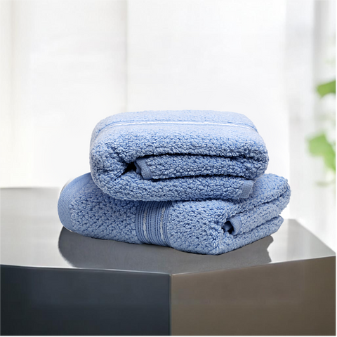 Two folded blue hand towels on a flat surface, with a plant in the background.