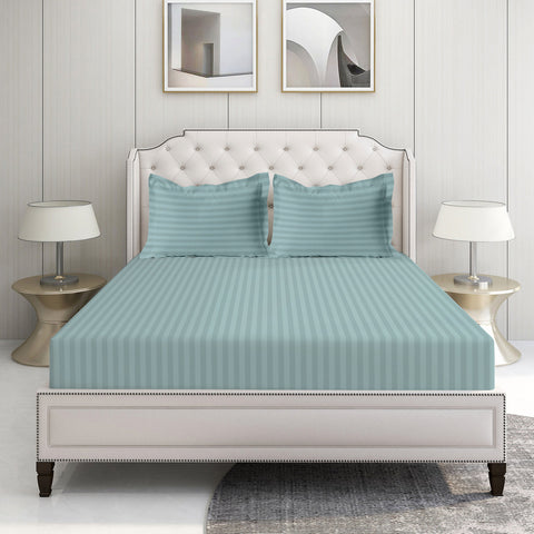 A set of blue striped bed sheets displayed on a bed in a room with a white headboard and a nightstand with a lamp on the side.