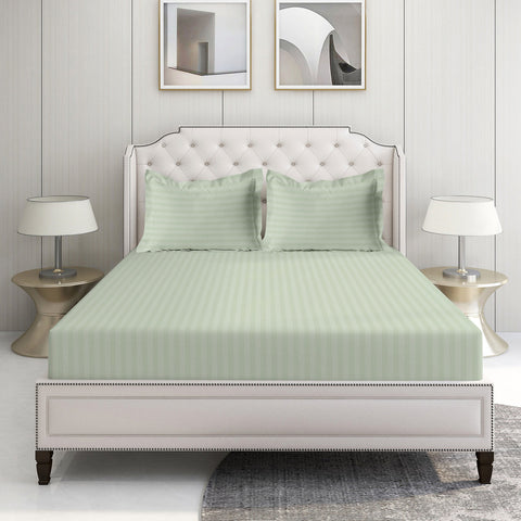 A king-sized sheet set with stripes, in a satin finish, displayed on a bed in a room with two framed pictures on the wall and a lamp on each side.
