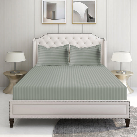 A king-size fitted sheet set with a silver stripe design, displayed on a bed in a room with two framed artworks on the wall and a nightstand with a lamp on the side.