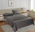 A charcoal gray king flat satin bedsheet set on a bed in a room with a tan headboard and a nightstand with a lamp and a plant beside the bed.