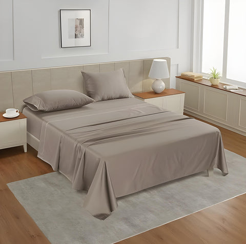 A taupe-colored king flat satin bedsheet set on a bed in a room with a tan headboard and a nightstand, with a lamp and a framed picture on the wall.
