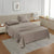 A taupe-colored king flat satin bedsheet set on a bed in a room with a tan headboard and a nightstand, with a lamp and a framed picture on the wall.