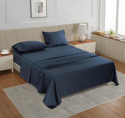 A queen-sized fitted satin sheet set in a Denim color with 2 Pillows displayed on a bed with a pair of pillowcases, in a room with a wooden floor and a light gray carpet.