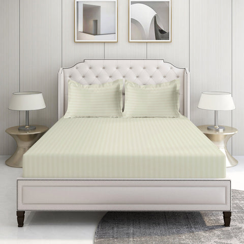 A set of ivory-colored Lane Linen 500TC 100% Organic Cotton bed sheets displayed on a bed in a room with two framed pictures on the wall and a nightstand with a lamp on the side.