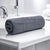 A rolled up gray bath towel placed on a white surface, likely a bathroom counter, with a faucet and partial view of a shower curtain in the background.