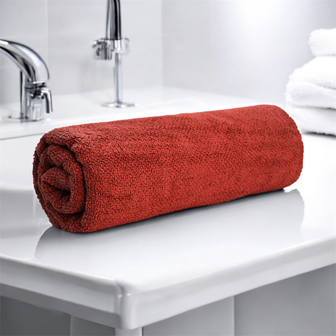 A rolled-up red cotton bath towel on a white surface in a bathroom setting.