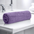 A rolled up purple bath towel placed on a white bathroom counter.