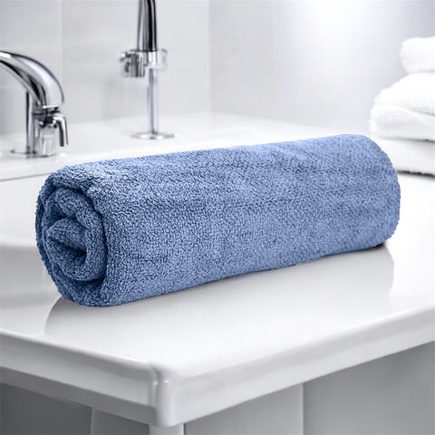 A rolled up light blue bath towel placed on a white bathroom counter.