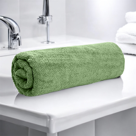 A rolled-up green cotton bath towel placed on a white surface in a bathroom setting.