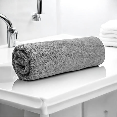 A rolled-up Silver cotton bath towel placed on a white surface in a bathroom setting.