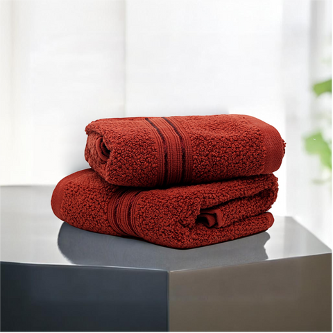 Two folded brown-colored cotton hand towels on a dark surface with a light background.