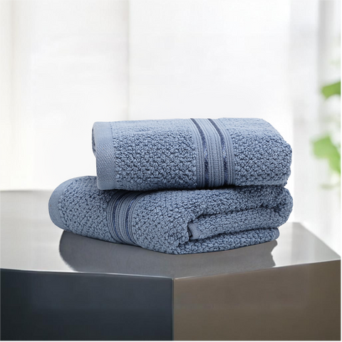 Two folded blue hand towels on a surface, with a plant in the background.