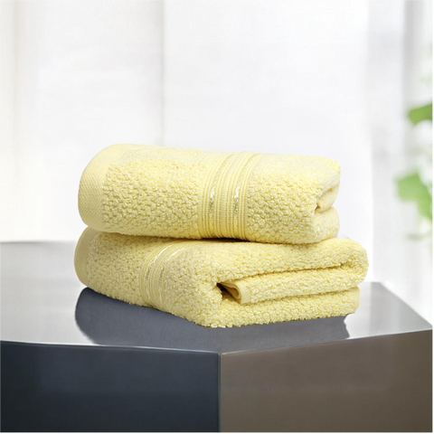 Two folded yellow hand towels on a surface with a window in the background.