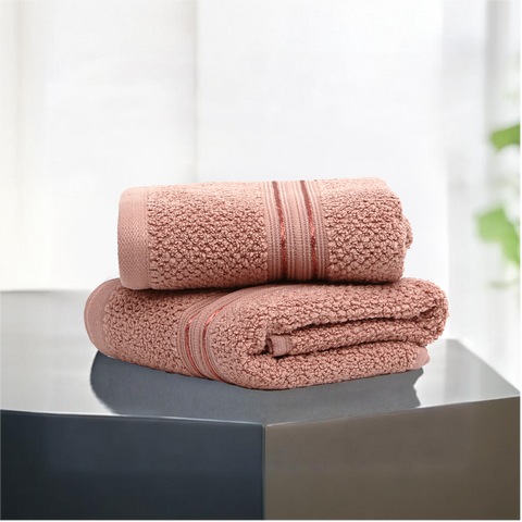 Two folded peach-colored cotton hand towels on a dark surface with a light background.