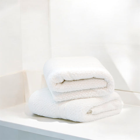 Two folded white hand towels on a shelf in a bright bathroom setting.