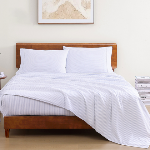 A set of white cotton bed sheets on a wooden bed frame, with a pillowcase displaying a solid pattern.