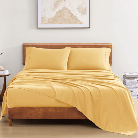 A set of yellow organic cotton bed sheets with a flat sheet and pillowcases displayed on a bed in a room with minimalist decor.